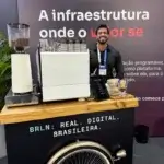 Barista masculino da Bom Café Eventos sorridente atrás de um carrinho de café com máquina de expresso branca da La Spaziale durante a ativação BRLN.