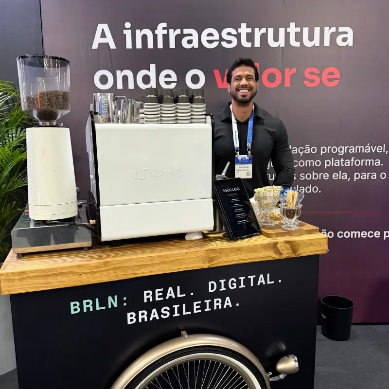 Barista masculino da Bom Café Eventos sorridente atrás de um carrinho de café com máquina de expresso branca da La Spaziale durante a ativação BRLN.