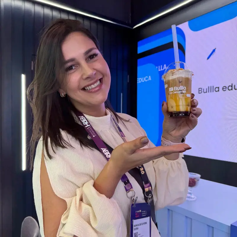 Visitante sorridente exibindo um copo de café gelado com caramelo personalizado da ação "Bullla no CONARH", feito pela Bom Café Eventos.